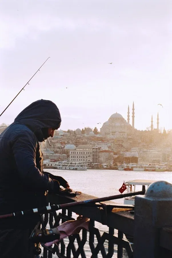 A hooded figure sketching the city from a ferry